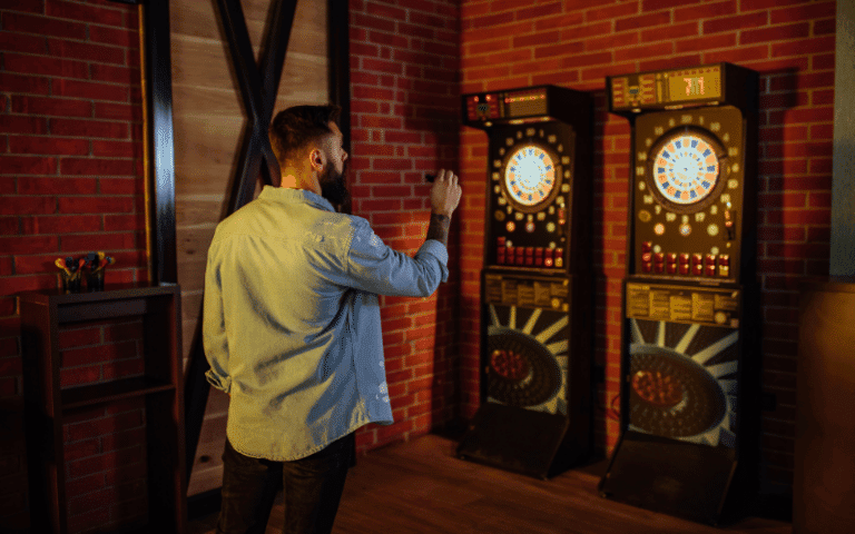 Players throwing darts at a board with numbered sections and a bullseye, surrounded by spectators and a scoreboard